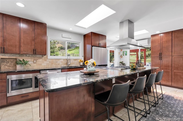 kitchen with a center island, a kitchen bar, a sink, island range hood, and appliances with stainless steel finishes