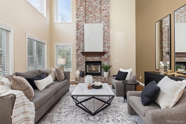 living area featuring wood finished floors, baseboards, a brick fireplace, and a high ceiling