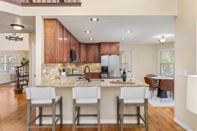 kitchen featuring a peninsula, appliances with stainless steel finishes, a sink, and light wood-style flooring