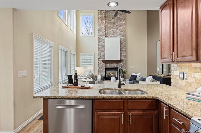 kitchen with a healthy amount of sunlight, a fireplace, light stone counters, a sink, and dishwasher