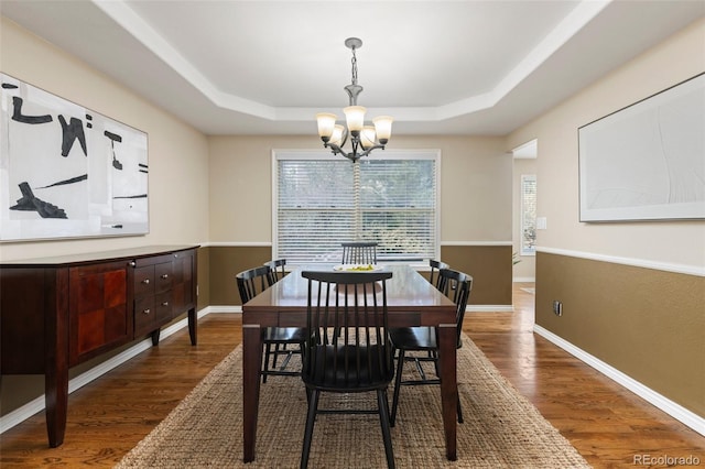 dining room with an inviting chandelier, dark wood finished floors, and a raised ceiling