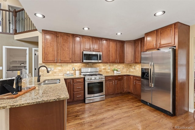 kitchen featuring brown cabinets, light stone counters, a sink, stainless steel appliances, and a peninsula