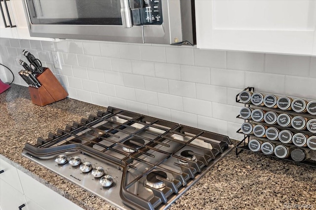 room details featuring stainless steel appliances, dark stone counters, white cabinets, and backsplash