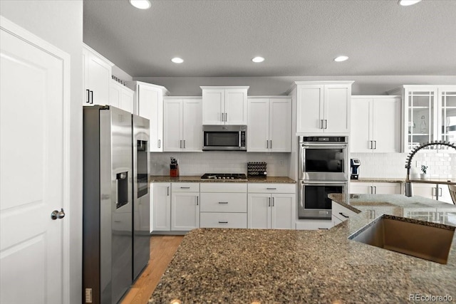 kitchen featuring a sink, white cabinetry, appliances with stainless steel finishes, backsplash, and light wood finished floors