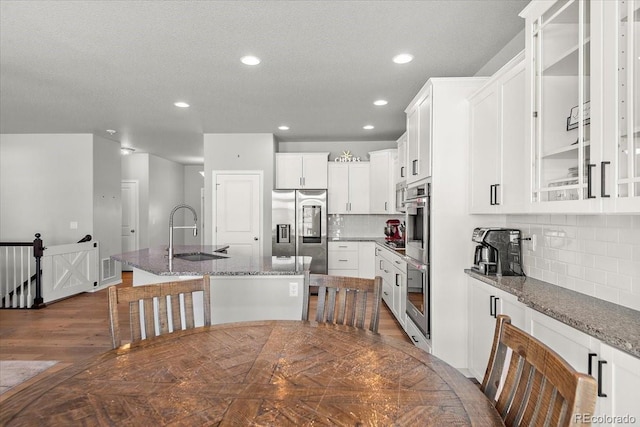 kitchen with a center island with sink, stainless steel appliances, stone countertops, white cabinetry, and a sink