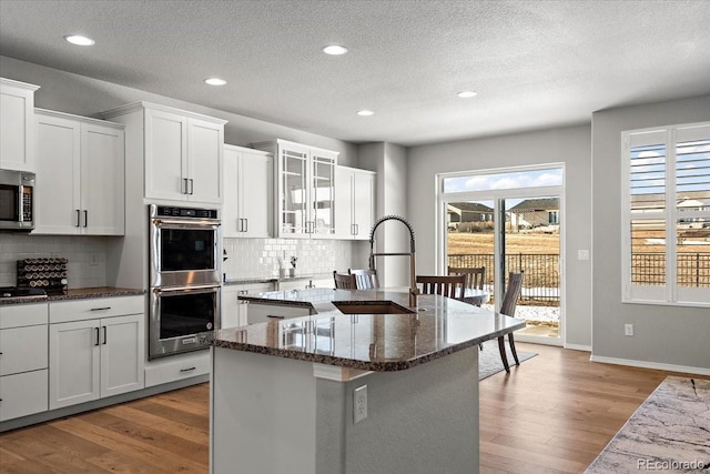 kitchen with a center island with sink, dark stone countertops, wood finished floors, stainless steel appliances, and a sink