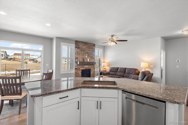 kitchen with a wealth of natural light, open floor plan, stainless steel dishwasher, and a stone fireplace