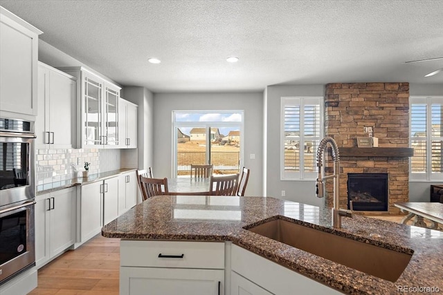 kitchen with tasteful backsplash, dark stone countertops, stainless steel double oven, a fireplace, and a sink