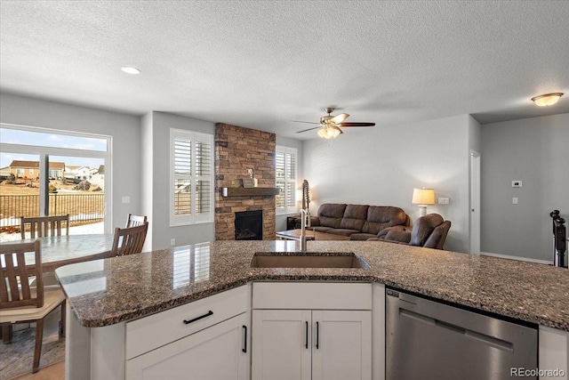 kitchen with open floor plan, stainless steel dishwasher, a fireplace, and a sink