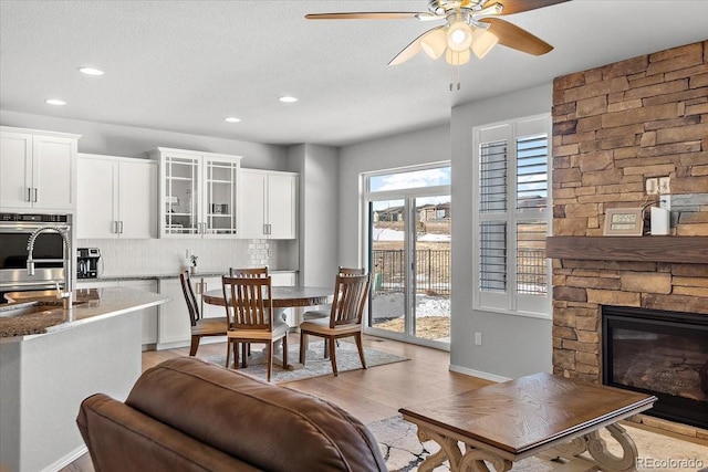 dining space with a textured ceiling, recessed lighting, a fireplace, a ceiling fan, and light wood finished floors