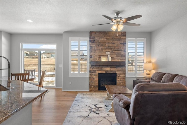 living room with a textured ceiling, a fireplace, wood finished floors, and a healthy amount of sunlight