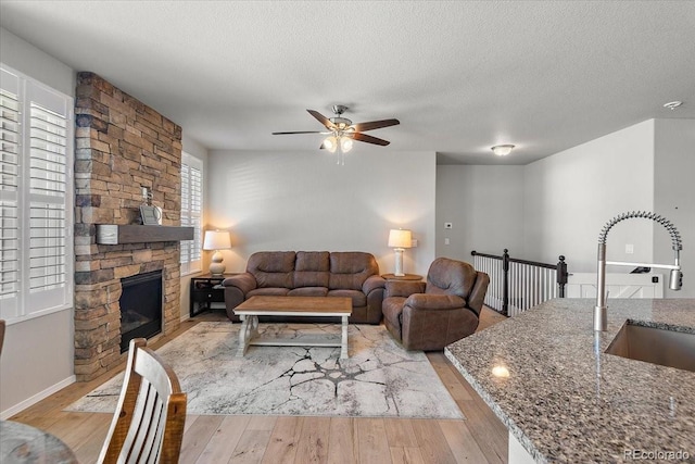 living room with light wood finished floors, ceiling fan, a textured ceiling, and a stone fireplace