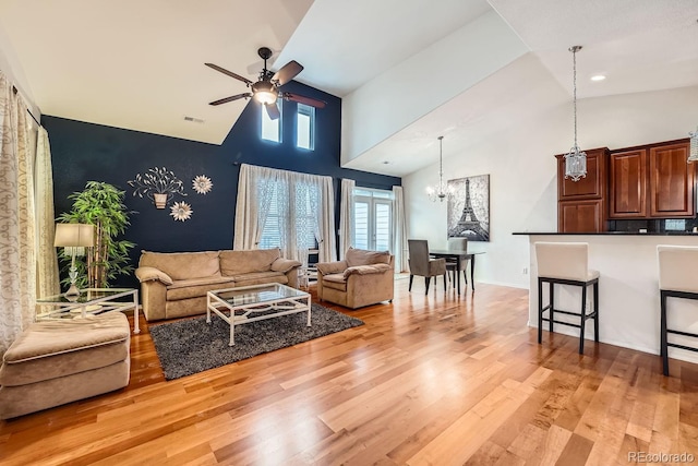 living room with high vaulted ceiling, ceiling fan with notable chandelier, and light hardwood / wood-style floors