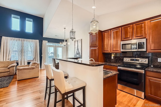 kitchen featuring a breakfast bar, appliances with stainless steel finishes, hanging light fixtures, dark stone counters, and light wood-type flooring