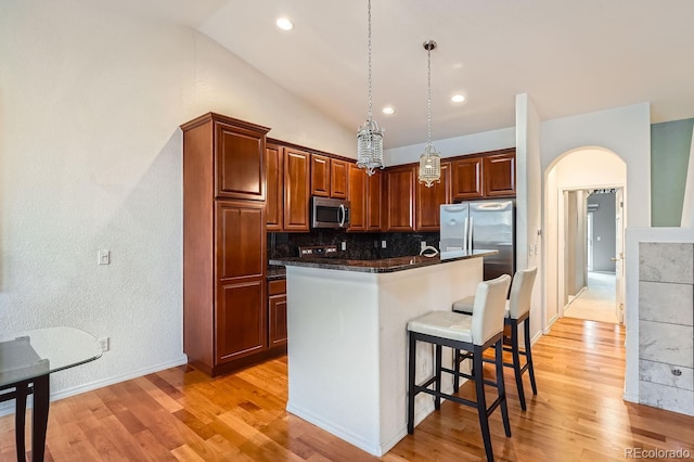 kitchen with decorative light fixtures, vaulted ceiling, a kitchen breakfast bar, a kitchen island, and stainless steel appliances