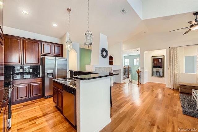 kitchen featuring vaulted ceiling, sink, stainless steel appliances, a center island with sink, and light hardwood / wood-style flooring