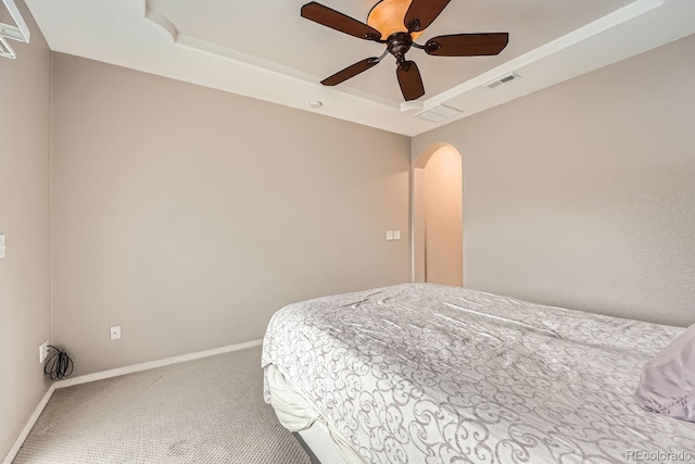 carpeted bedroom with a raised ceiling and ceiling fan