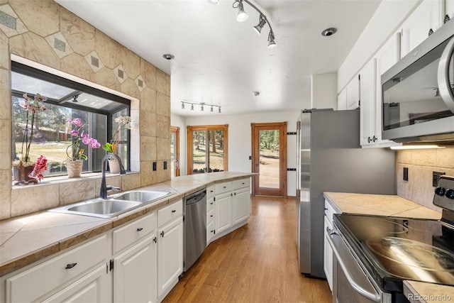 kitchen with appliances with stainless steel finishes, sink, light hardwood / wood-style floors, white cabinetry, and tile counters