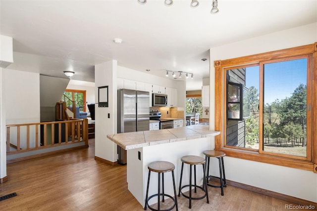 kitchen featuring kitchen peninsula, appliances with stainless steel finishes, white cabinetry, and a healthy amount of sunlight