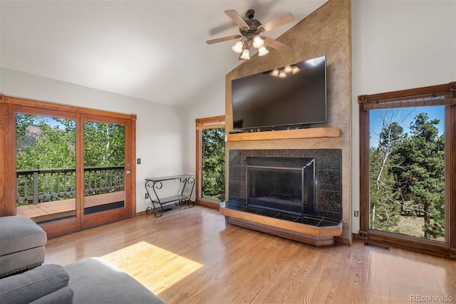 living room featuring hardwood / wood-style flooring, ceiling fan, high vaulted ceiling, and a tile fireplace