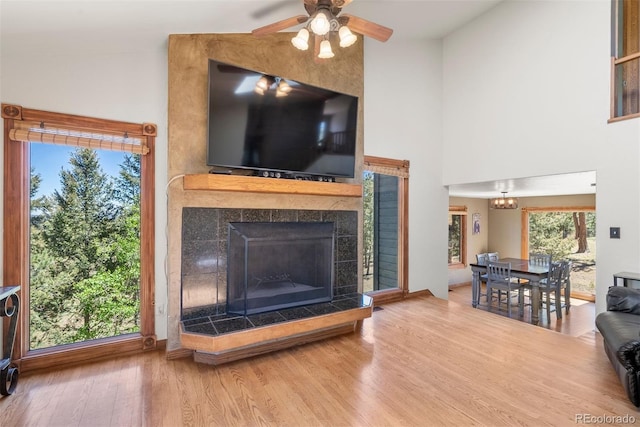 living room with a tiled fireplace, hardwood / wood-style floors, high vaulted ceiling, and ceiling fan with notable chandelier