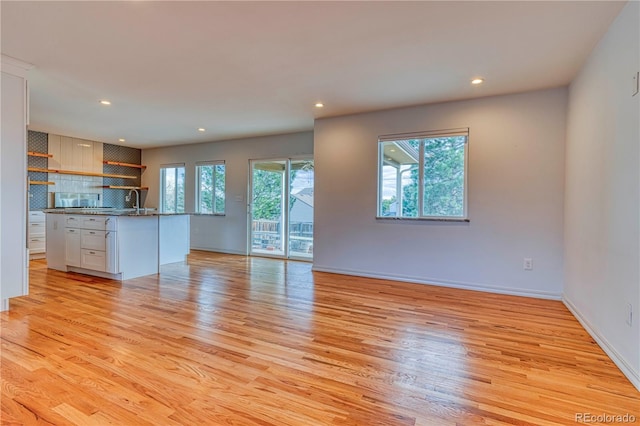 unfurnished living room with light wood-type flooring, baseboards, a sink, and recessed lighting