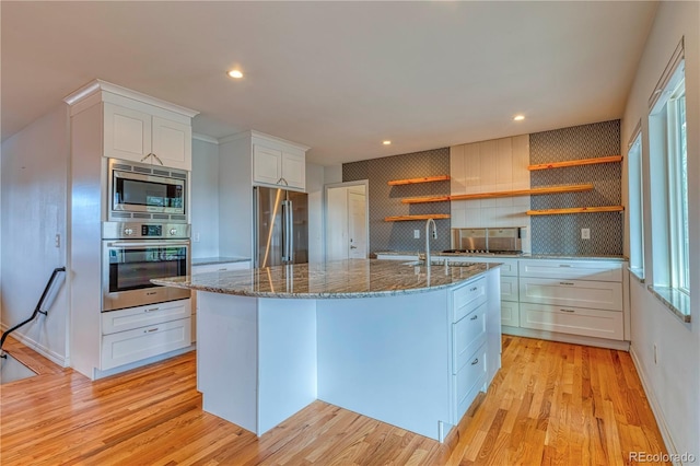 kitchen featuring stainless steel appliances, white cabinets, a center island with sink, and open shelves