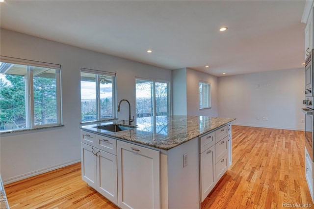 kitchen featuring stone countertops, a sink, white cabinetry, light wood finished floors, and a center island with sink