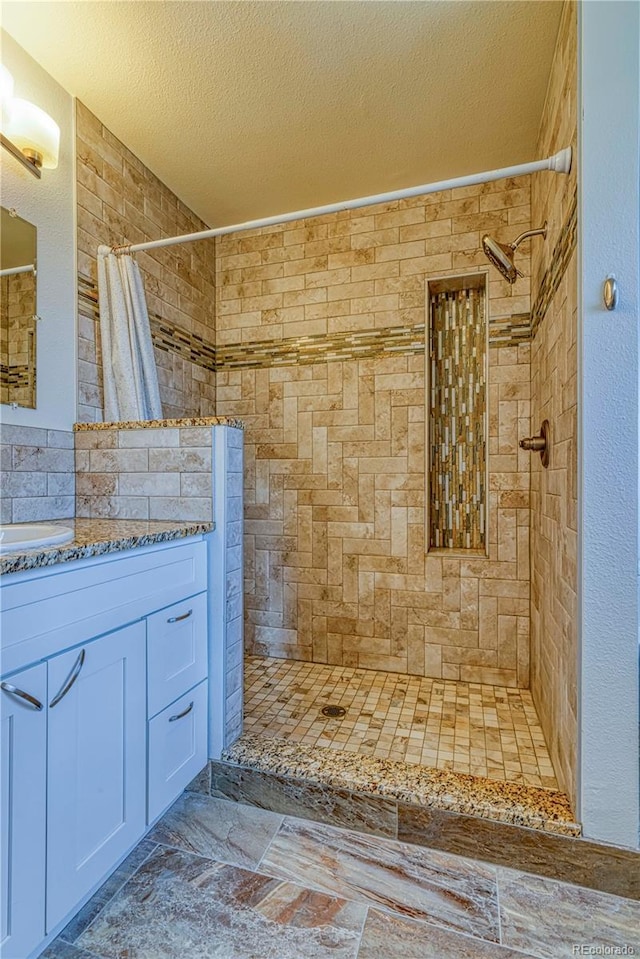 full bathroom featuring a textured ceiling, tiled shower, and vanity