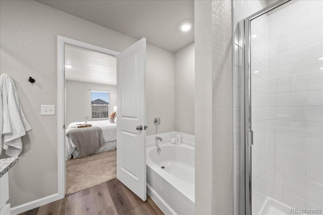 ensuite bathroom with baseboards, wood finished floors, ensuite bathroom, a shower stall, and a bath