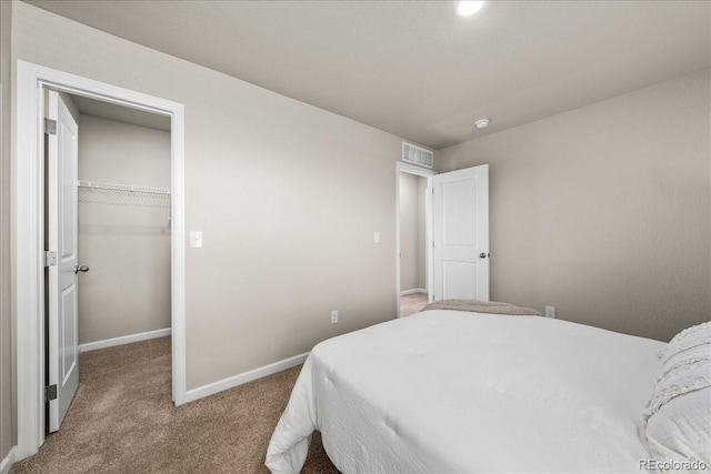 carpeted bedroom featuring a walk in closet, a closet, visible vents, and baseboards