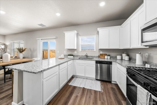 kitchen with stainless steel appliances, a peninsula, a sink, visible vents, and white cabinetry