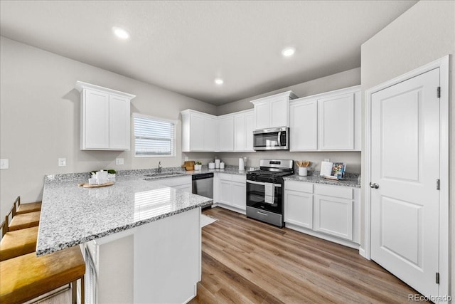 kitchen with white cabinets, a breakfast bar area, a peninsula, stainless steel appliances, and a sink