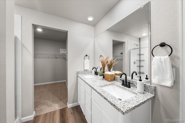 bathroom featuring a walk in closet, tiled shower, a sink, and wood finished floors