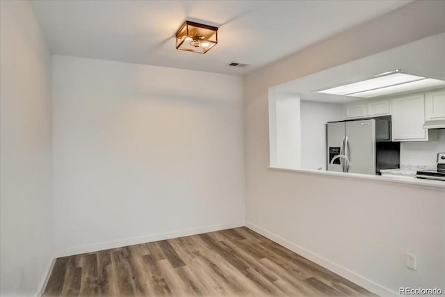 interior space with light hardwood / wood-style floors, stainless steel fridge with ice dispenser, range, and white cabinetry