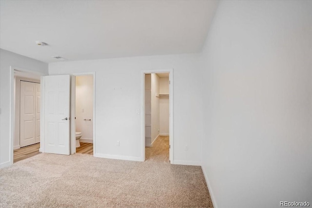 unfurnished bedroom with light carpet, a spacious closet, a closet, and connected bathroom