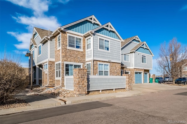 view of front of home with driveway, a garage, stone siding, a fenced front yard, and board and batten siding