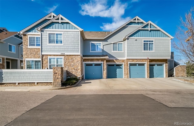 townhome / multi-family property featuring stone siding, fence, board and batten siding, concrete driveway, and a garage