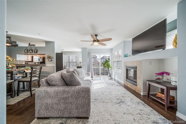 living room with baseboards, dark wood-type flooring, a ceiling fan, and a tile fireplace