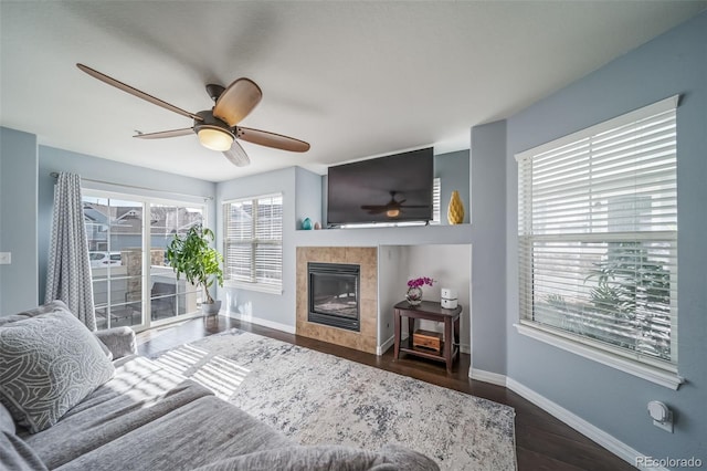 living room with a ceiling fan, wood finished floors, baseboards, and a tile fireplace