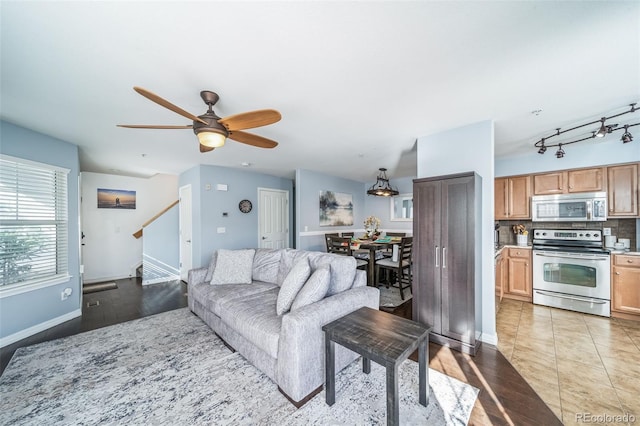 living area with light tile patterned floors, stairway, ceiling fan, and baseboards