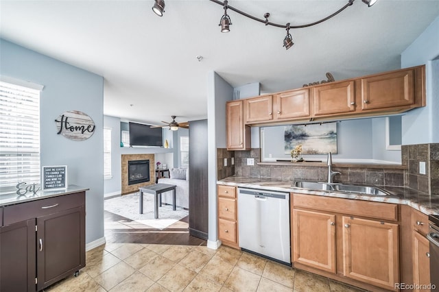 kitchen featuring a sink, stainless steel dishwasher, decorative backsplash, ceiling fan, and a tile fireplace