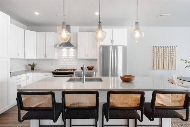 kitchen with visible vents, a sink, appliances with stainless steel finishes, wall chimney range hood, and backsplash