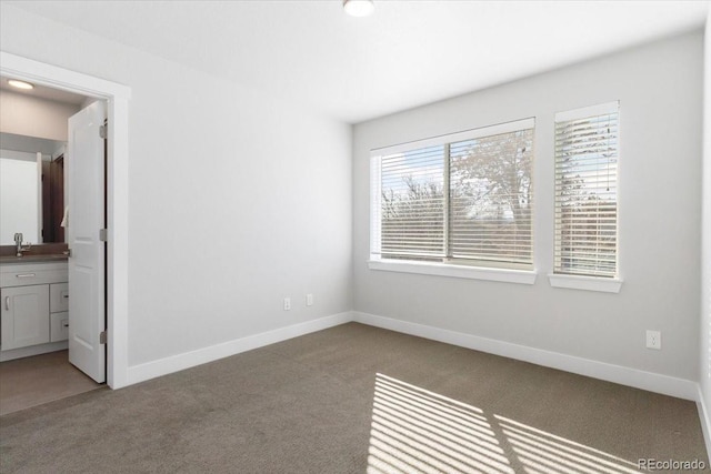 unfurnished bedroom with a sink, baseboards, carpet floors, and ensuite bathroom