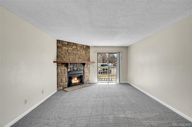 unfurnished living room featuring carpet flooring, a textured ceiling, a stone fireplace, and baseboards