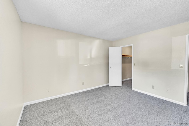 unfurnished bedroom with a textured ceiling, a closet, carpet flooring, baseboards, and a spacious closet