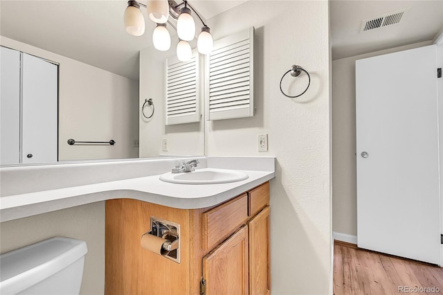 half bath with visible vents, toilet, wood finished floors, and vanity