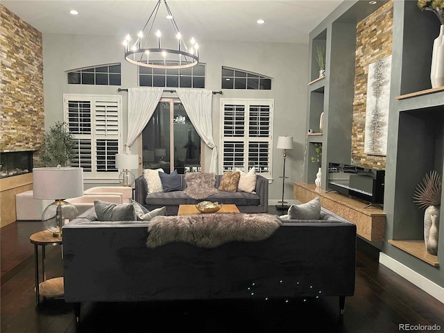 living room with dark wood-type flooring, a high ceiling, a stone fireplace, built in features, and a notable chandelier