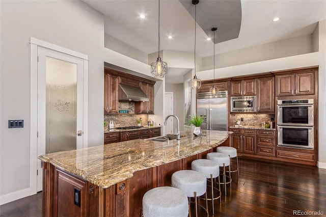 kitchen with built in appliances, decorative light fixtures, sink, and range hood