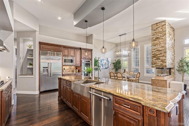 kitchen featuring sink, a stone fireplace, dark hardwood / wood-style floors, built in appliances, and a spacious island